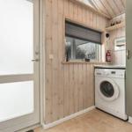 Waschmaschine in einem Raum mit Holzwand und Fenster. Tür und Kleidungsstück sind sichtbar.