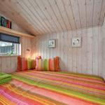 Schlafzimmer mit Holzwänden, Bett mit buntem Bettzeug und Fenster mit Jalousie.