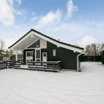 Schwarzes Holzhaus mit weißem Dach und Schneebedecktem Grundstück.
