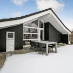 Moderne Holzhütte mit großem Terrassenbereich und Sitzgelegenheiten im Schnee.