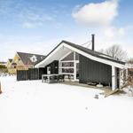 Schwarzes Haus mit weißem Dach und Terrasse im Schnee.