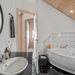 Bathroom with bathtub, sink, and mirror. Wooden ceiling and white walls.