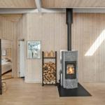 Living room with wood stove, firewood stack, and glass cabinet. Bedroom in background.