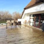 Terrasse mit Tisch und Stühlen, Grill und Glasfront zur Unterkunft.