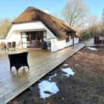 Haus mit Strohdach und Holzterrasse mit Gartenmöbeln und Reste Schnee.