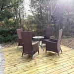 Terrasse mit vier Stühlen und Tisch, umgeben von Bäumen und Sand.