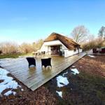 Haus mit strohgedecktem Dach und großer Holterrasse mit Sitzgelegenheiten.