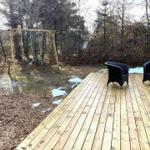 Holzterrasse mit zwei schwarzen Sesseln und Schaukel im Wald.