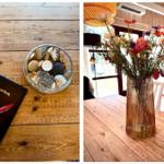Gästebuch und Steinbecher auf Holztisch. Blumenarrangement auf Tisch mit Sofa im Hintergrund.