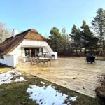 Haus mit Strohdach und großer Holterrasse mit Tisch und Stühlen.