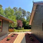 Holzhaus mit Terrasse und Garten, umgeben von Bäumen und Blumenbeeten.