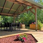 Holzterrasse mit Sitzgruppe, Grill und Pflanzenbeeten unter Dach