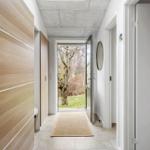 Hallenflur mit Holzschrank, Tür zum Garten und runder Wandspiegel.