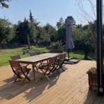 Holzterrasse mit Tisch, Stühlen und Sonnenschirm. Grünfläche und Bäume im Hintergrund.