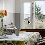 Tisch mit Blumen, Tasse und Zeitschrift vor Fenster mit Blick nach draußen.