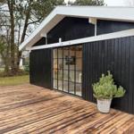 Moderne Hütte mit Holzterrasse und Glasfront. Pflanze im Korb steht vor der Wand.