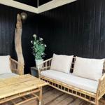 Terrasse mit Bambusmöbeln, Sitzbank und Tisch. Schwarze Holzwand und Pflanze im Hintergrund.