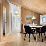 Dining area with round table and chairs, wooden walls and floor, windows with curtains.