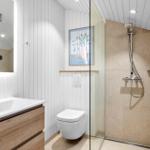 Bathroom with shower, sink, and toilet. Wall cladding and floor tiles.