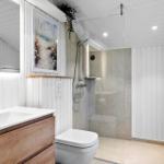 Bathroom with shower, sink, and toilet. White walls and wood accents.