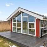 Modern villa with large wooden deck and glass facade. Outdoor table and seating area.