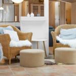 Two wicker chairs with cushions and fur throws stand on terracotta floor.