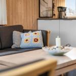 A living area with a gray sofa, wooden furniture, and a kitchen counter in the background.