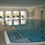 Innere Schwimmhalle mit Pool, Liegestühlen und Glasfronten.