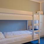 Zimmer mit Doppelstockbett, Kleiderschrank und Fenster.