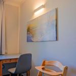 Schreibtisch mit zwei Stühlen und Kinderhochstuhl an Wand mit Strandbild.