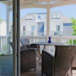Terrasse mit Tisch und Stühlen, Blick auf weiße Häuser und Bäume.