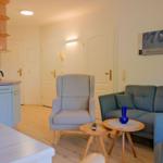 Wohnbereich mit Sofa, Sessel und Küchenzeile. Holzboden und Wandbilder.