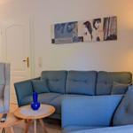 Wohnzimmer mit Sofa, Sessel und Tisch. Wandbild und Stehlampe sichtbar.