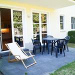 Terrasse mit Tisch, Stühlen und Liegestuhl. Durchgang ins Haus. Grünflächen umgeben.