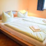 Doppelbett mit Bettwäsche und Handtüchern, Nachttisch mit Lampe, Fenster mit Vorhang.