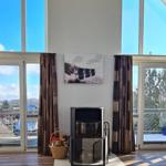 Großes Wohnzimmer mit Kamin und hohen Fenstern. Holzboden und Vorhänge.