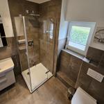 Badezimmer mit Dusche, Waschbecken und Toilette. Fenster mit Blick auf Grün.