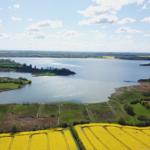 Aerial view of a large lake surrounded by green fields and yellow rapeseed.