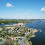 Luftbild einer Küstenlandschaft mit Häusern, Feldern und einem Hafenbecken.