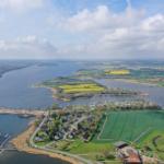 Luftbild einer idyllischen Landschaft mit Fluss, Bootshäfen und grünen Feldern.