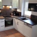 Küche mit weißen Schränken, dunkler Arbeitsplatte und Fenster mit Blick nach draußen.