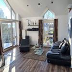 Wohnzimmer mit schwarzem Sofa, Glas-Tisch und großen Fenstern.