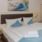 Doppelbett mit blauen Kissen und Bettwäsche, Wandbild mit Strandhut, Nachttische mit Lampen.