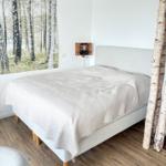 Schlafzimmer mit Bett, Wandbild und Birkenstämmen.