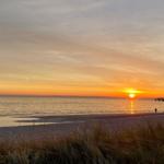 Sonnenuntergang über dem Meer mit Strand und Dünen im Vordergrund.