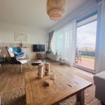 Wohnzimmer mit Holzboden, Sitzgelegenheiten und großem Fenster zum Balkon.