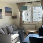 Wohnzimmer mit Sofa, Tisch und Fenster. Wandbilder zeigen Küstenlandschaften.