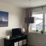 Wohnzimmer mit Fernseher, Wandbild und Fenster mit Pflanzen.