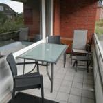 Terrasse mit Glas-Tisch und Stühlen, roter Backsteinwand, Blick auf Grünfläche und Straße.