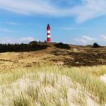 Roter Leuchtturm auf Dünen mit Gras und blauem Himmel.